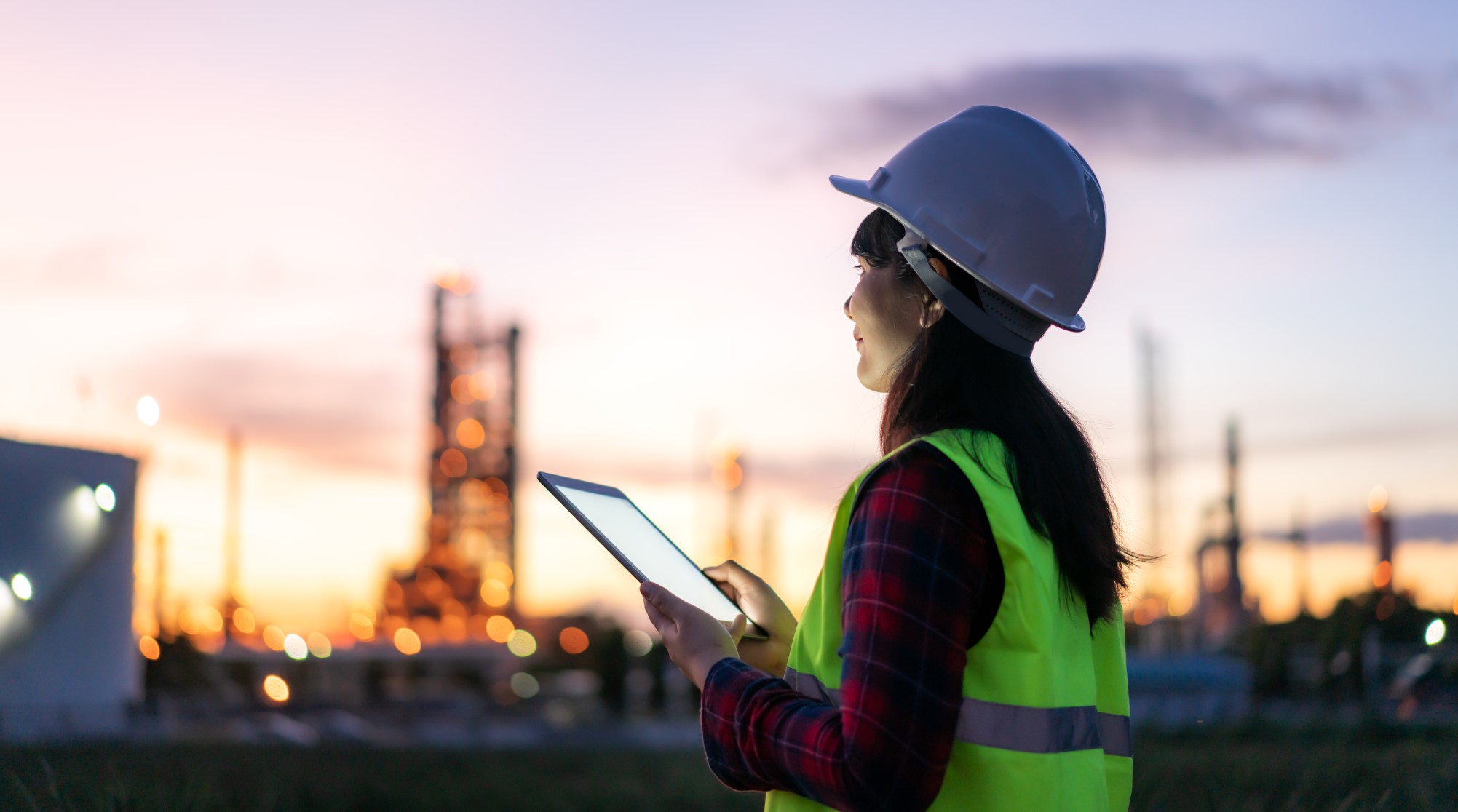 Woman holding tablet at construction site while the sun is setting.